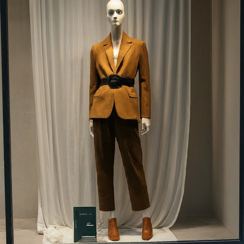Black belt worn around the waist of a women's suit pants, leading down to brown leather shoes.