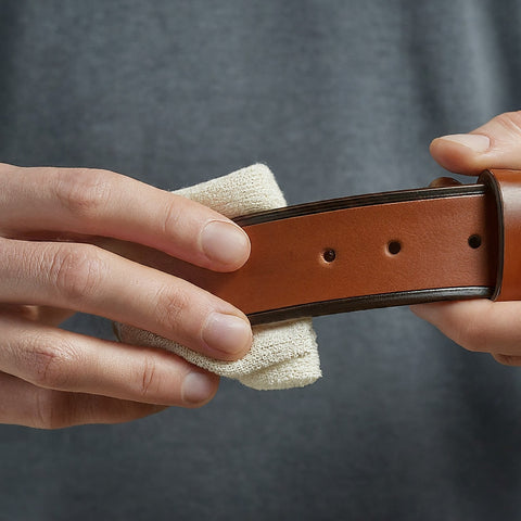 Applying leather conditioner to a belt with a soft cloth for maintenance.