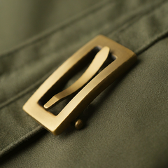 Close-up of a bold, rectangular belt buckle made of brushed brass with a single, thick prong, inspired by military designs.