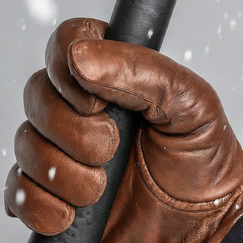 Close-up of a person wearing brown winter leather gloves holding a hammer in the snow, showcasing control and comfort in cold weather.