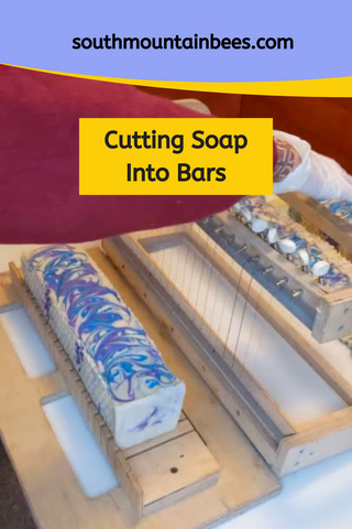 Cold process soap loaf with purple and blue swirls on wooden cutter ready to be sliced into bars. 