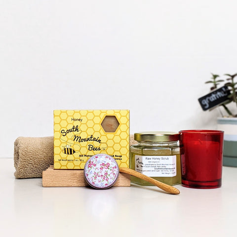 Candle light gift set with an assortment of bath and body products and a beeswax candle on a red glass votive holder.