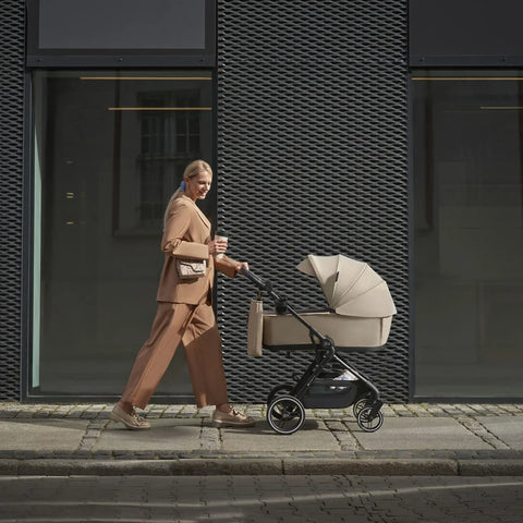 A woman holding a cup and pushing the New Kinderkraft Stroller YOXI