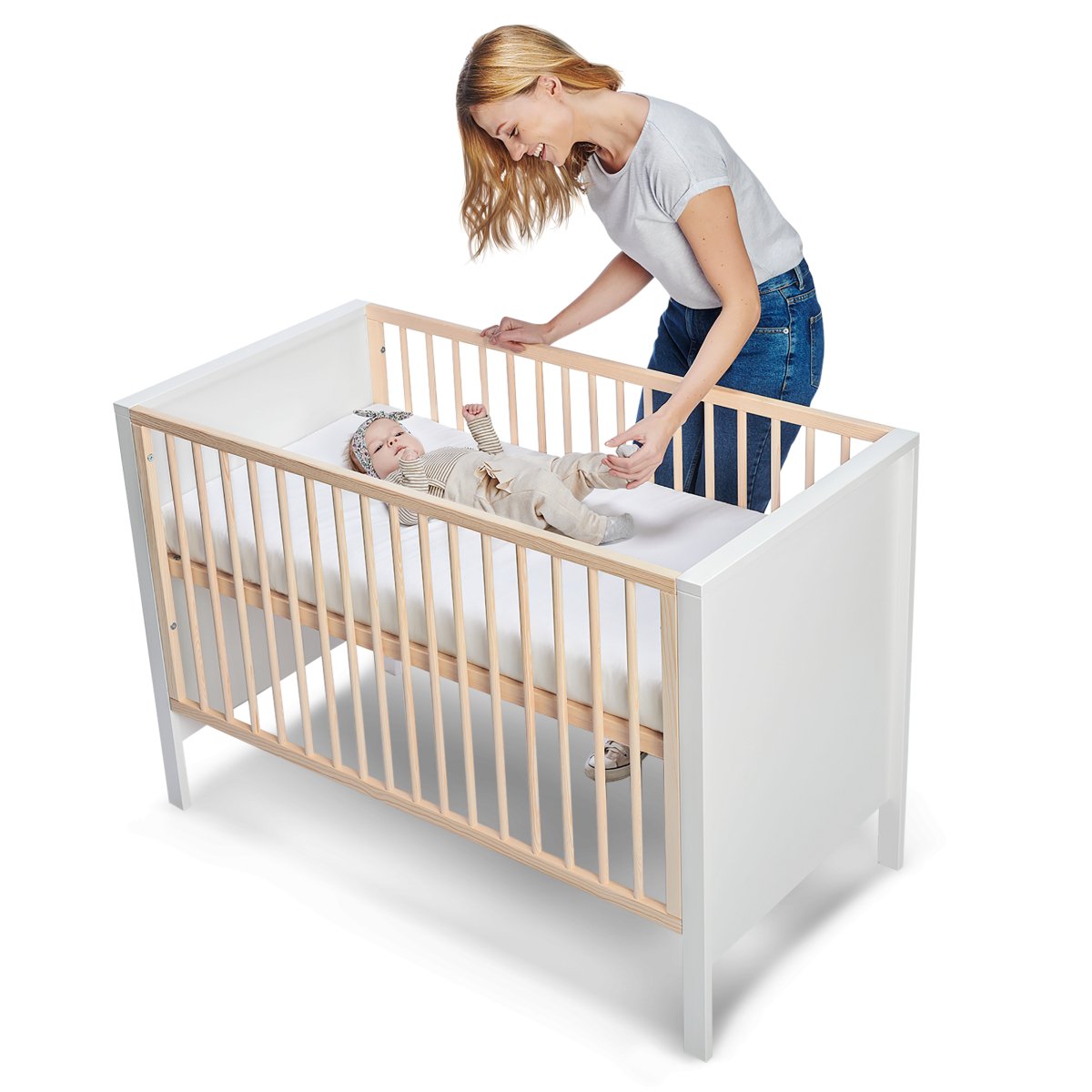 Mother tucking baby into Kinderkraft Baby Cot MIA with mattress.