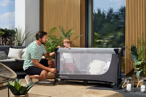 Father and child interacting beside Kinderkraft Travel Cot LEODY outdoors