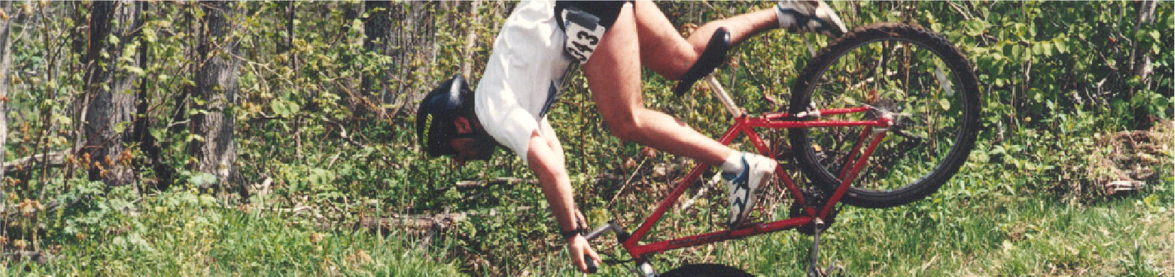 Photo of a man crashing on his bike, suspended in the air on his front wheel before the fall.