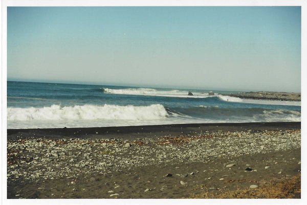 Photo of breaking waves on the beach with tiny surfers barely visible on the waves.