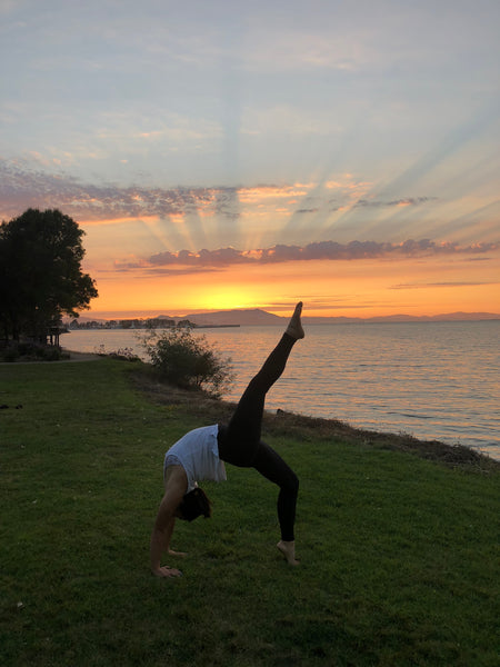 Margaret in a bridge pose with one leg up and a sunset behind her.