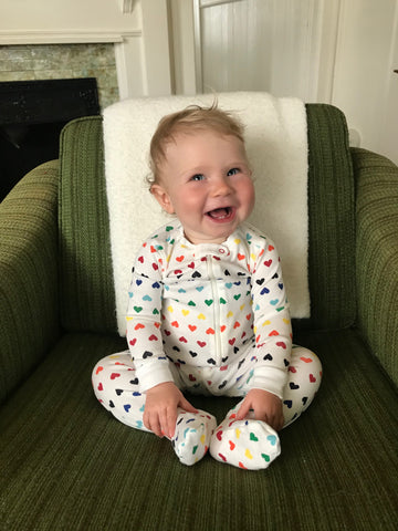 Noa sitting on a chair wearing a rainbow-heart onesie.