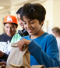 Child with brown paper bag lunch.