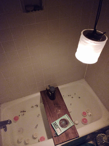 Rachel's bath full of citrus peels, a book on a plank of wood over the bath tub, and a lantern hanging over head.