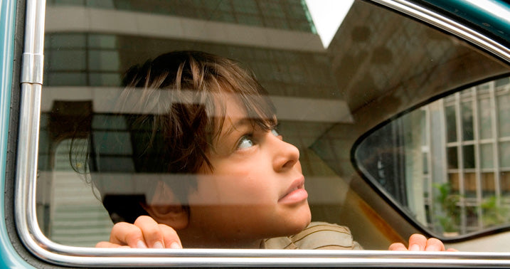  menino olhado pela janela traseira de um fusca azul em cena do filme o ano em que meus pais saíram de férias