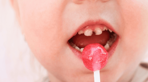 Toddler with dirty plaque-filled teeth eating a red sucker