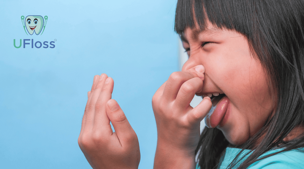 Young girl testing her breath against her hand while plugging her nose with the other against a light blue background