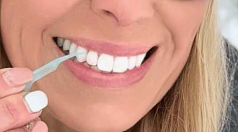 Middle-aged woman using UFloss dental flossing pick to clean her beautiful straight, white teeth