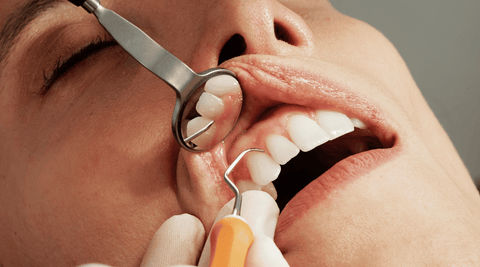 Woman receiving dental checkup from dental hygienist using dental pick and mirror tools