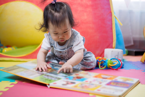 A toddler reading a board book on the floor