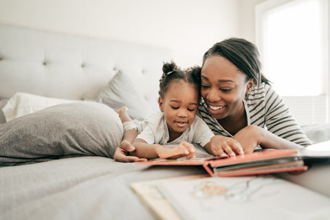 A mother reading a board book with their toddler in bed