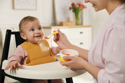 Baby wearing a yellow silicone bib being fed by her mother
