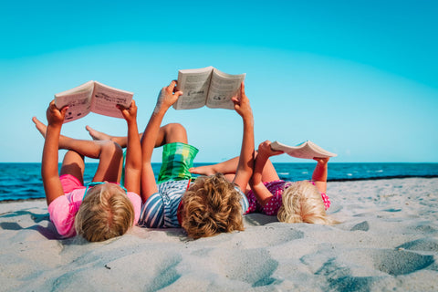 Kids reading on the beach during their family holiday