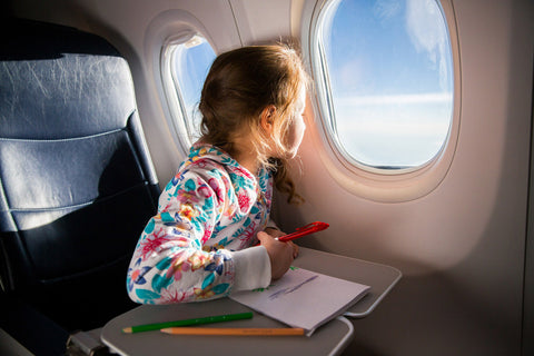 Girl looking out of the aeroplane window while drawing