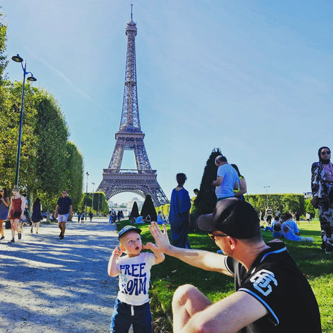 A toddler and his dad giving each other high five in front of the Eiffel Tower in Paris France