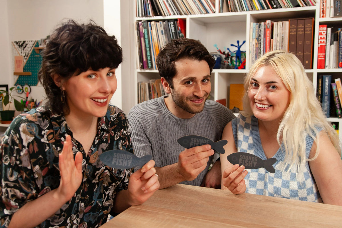 Three people holding up Sounds Fishy fishes