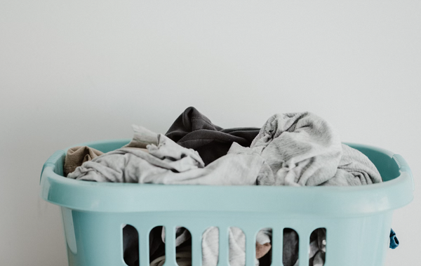 A light blue laundry basket overflowing with mess clothes.