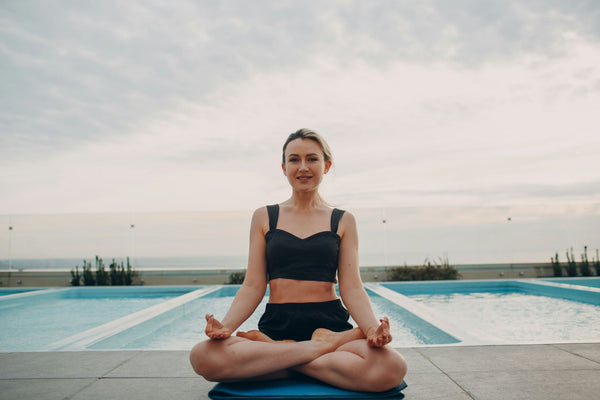 Woman sitting by the pool in a meditative pose, enjoying a calm moment and staying fresh with stick deodorant.