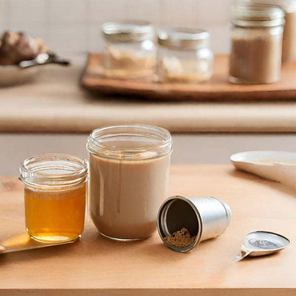 A kitchen setting with a freshly brewed cup of mushroom coffee, a measuring spoon with mushroom powder, and a small jar of honey on a wooden countertop.