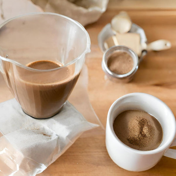 A cup of mushroom coffee being brewed with a coffee maker, with a bag of mushroom powder and a scoop nearby.