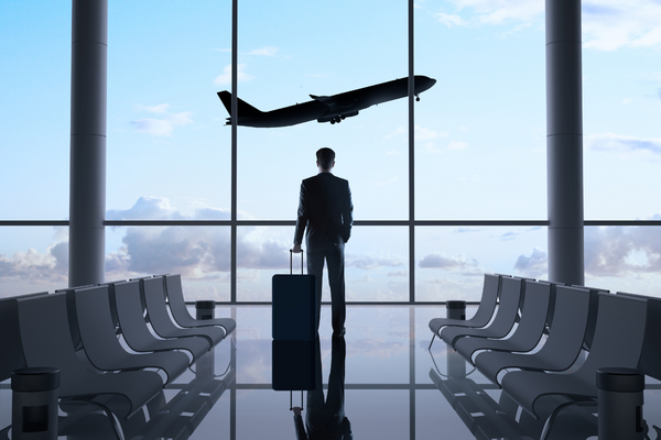 person standing at the airport departure gate with his suitcase watching a plane take off