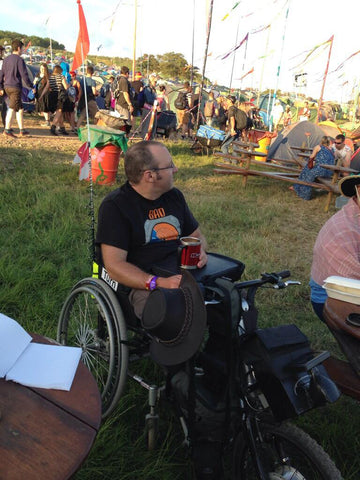 disabled man on a trike at a festival with a can of drink on a trabasack