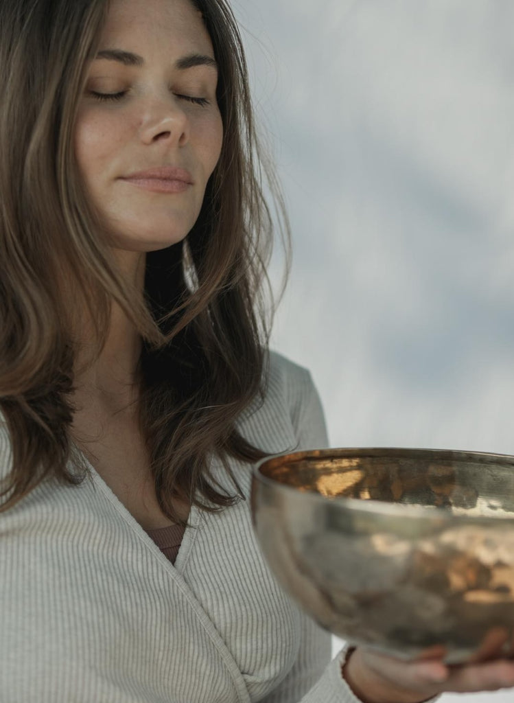 A girl is smiling with closed eyes and holds a sound bowl