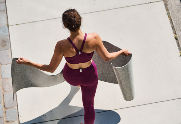 A woman is wearing pink yoga wear and holds the rather light hejhej-mat in her hands