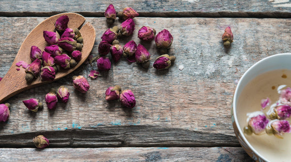 A wooden spoon on a table holding rose buds. 