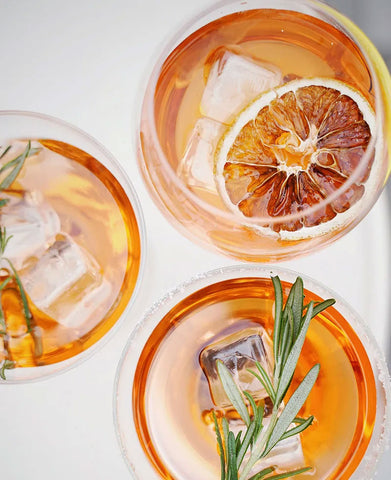 Sliced orange fruit, rosemary, and ice cubes in clear drinking glasses. Image by Olena Bohovyk