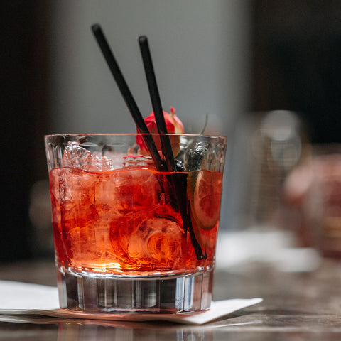 A red drink with ice in a clear glass with cherry garnish and cocktail straws. Photo by Pavel Danilyuk.