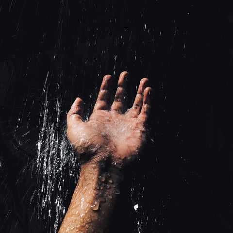 Water falls onto an opened hand in front of a black background. Image by Sachith Hettigodage, Unsplash.