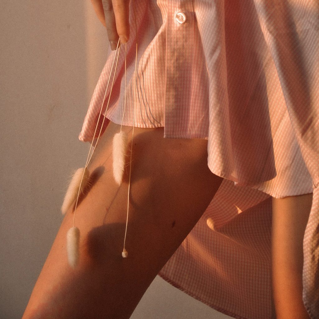 A woman in a pink dress holds soft stems agains her leg in the golden light.