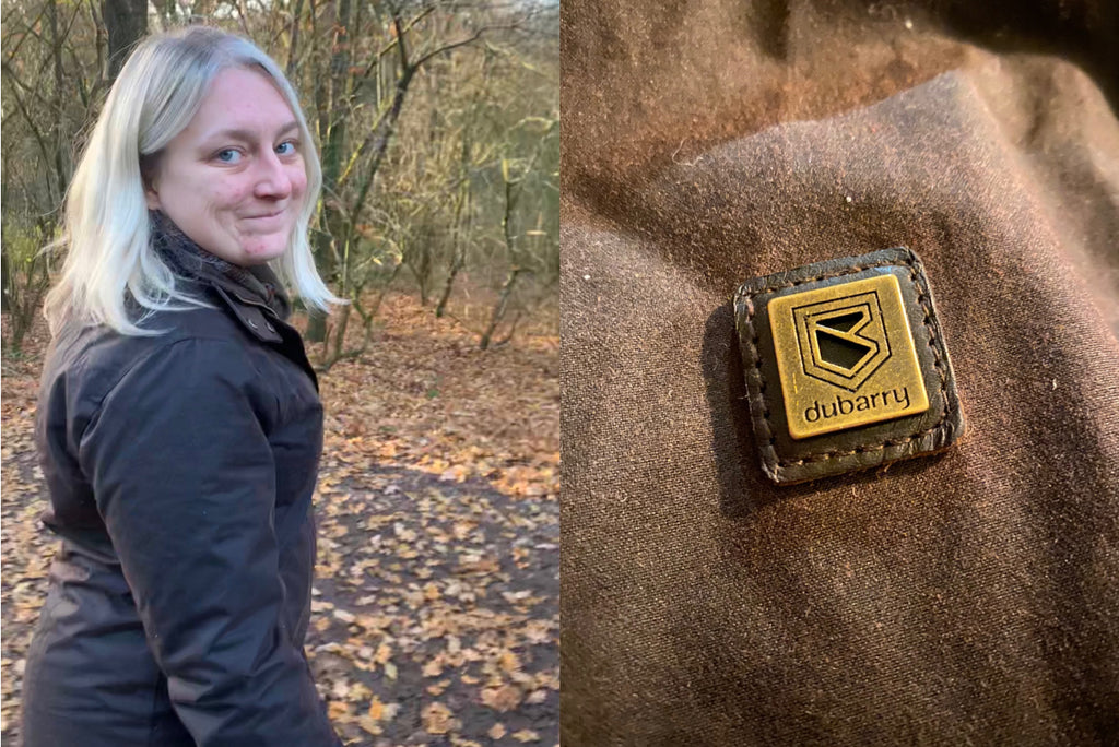 On the left is a midshot of a woman wearing a Mountrath Wax Jacket in a forest in an autumnal setting, with brown leaves on the ground and bare trees in the background. On the right is a close-up of the Dubarry broga logo embossed in gold.