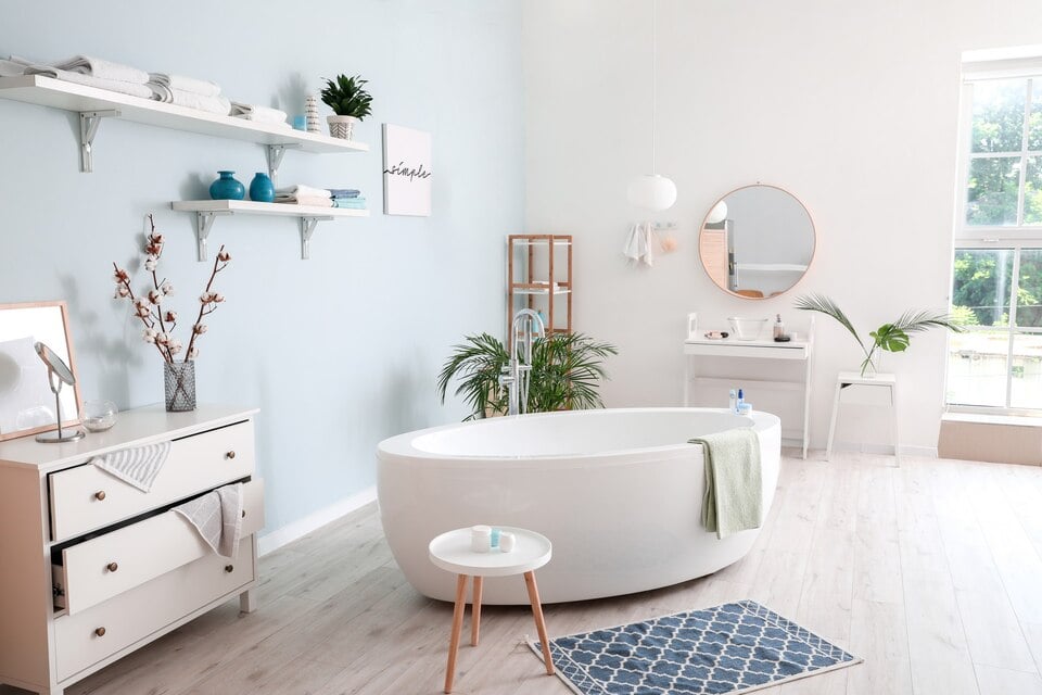 A clean bathroom with a white tub, a blue rug & a drawer