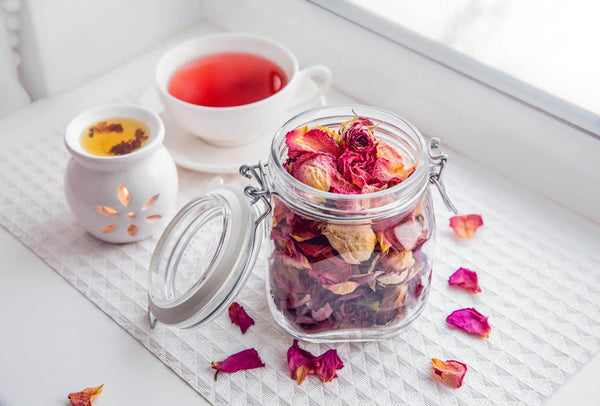 A glass jar filled with dry flowers alongside a cup containing teaA glass jar filled with dry flowers alongside a cup containing tea
