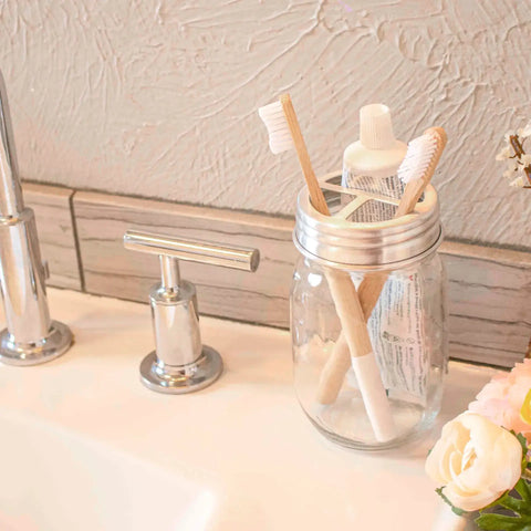 A glass jar with toothbrush in it sitting on a bathroom basin