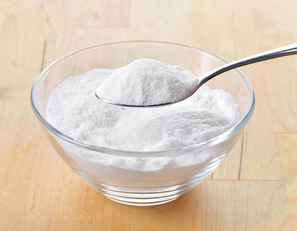 A spoon containing baking soda above a glass container filled with baking soda