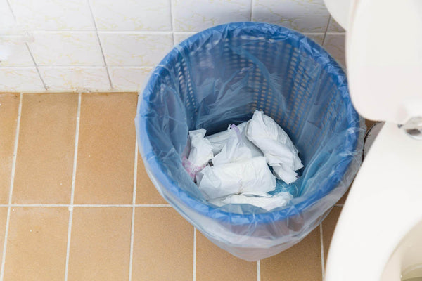 A dustbin in a bathroom containing trash