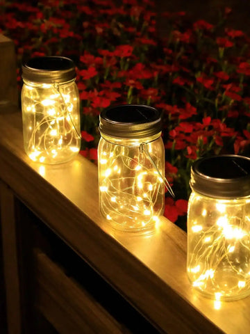 Three glass jars on a wooden railing with led lights inside them on