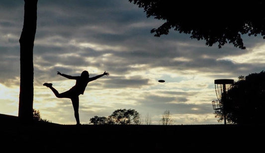 silhouette of disc golfer throwing into a basket 