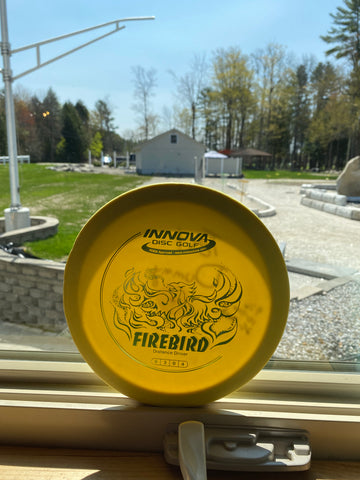 A yellow DX Firebird sitting in the widow at Sabattus Disc Golf, heating in the sun.