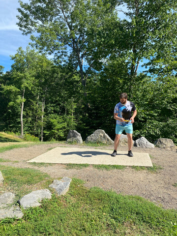 Blog writer and lesson instructor Andrew Streeter continues to demonstrate a disc golf X-Step drive by spinning his body to the left, bringing his right arm to the basket. 